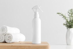 White cosmetic trigger sprayer bottle mockup with towels and a rosemary on a wooden table.