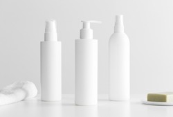 Set of white cosmetic bottles mockup with a towel and a natural soap on a white table.
