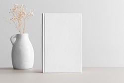 White book mockup with gypsophila in a vase on a beige table.