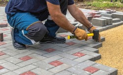 Professional bricklayers install new tiles or slabs for the roadway, sidewalks or patio on a foundation of lined sand. Laying gray concrete paving slabs in the courtyard of the house.