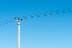 reinforced concrete pillar with high-voltage wires against a clear blue sky. Transmission of electricity by wires over long distances.