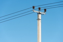 reinforced concrete pillar with high-voltage wires against a clear blue sky. Transmission of electricity by wires over long distances.