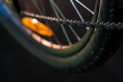 The orange reflector is mounted on the spokes of the rear wheel of a mountain bike. Various bike parts close-up in the workshop, studio orange light. Safe bike control.