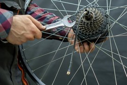 The bike mechanic installs a new cassette on the motor wheel. Repair of electric bicycles. Mechanic's hand and wrench close-up. Replacement of worn-out equipment on a mountain bike
