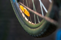 The orange reflector is mounted on the spokes of the rear wheel of a mountain bike. Various bike parts close-up in the workshop, studio orange light. Safe bike control.