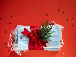 Hygienic face masks as a gift with a red ribbon, Christmas and New Year 2021 decor on a red background with space for text. Holidays self-isolation and coronavirus pandemic concept