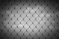 Black and White Image of a Chain Link Fence against a Cloudy Sky with Vignette