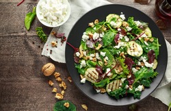 Grilled Zucchini salad with feta cheese, walnut nuts and glass of red wine in a black plate on wooden table