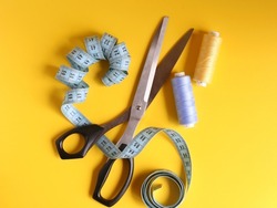 Blue Measuring Ruler Sewing, tailor's scissors with a black handle and two spools of thread. Yellow background, top view
