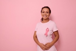 A smiling mixed race woman in pink T-shirt with pink satin ribbon symbolizing International Breast Cancer Day, expressing solidarity and support for breast cancer patients and survivors. 1 st october