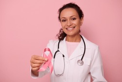 Beautiful African American female doctor with beautiful toothy smile showing a Pink satin Ribbon, isolated on colored background with copy space. World Day of fight Breast Cancer, 1 st October concept