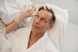 Men's cosmetology. Beautician injects a botulinum toxin into a man's forehead to relax the muscles. Mature man receiving facial rejuvenation injection procedure for smoothing and anti-aging therapy