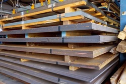 Steel sheets in warehouse, rolled metal product. Sheets of metal are stacked on a pallet. Many pallets of sheet metal of different thicknesses are stacked on top of each other.