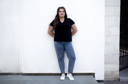 Beautiful plump woman wearing jeans and t-shirt posing against the street wall in the city