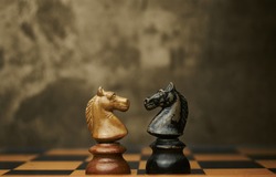 Wooden chess pieces knights facing each other on a vintage chessboard. Confrontation and rivalry concept, selective focus.