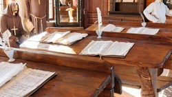 Learning to read and write in the middle ages concept. A classroom with wooden desks containing parchment, scrolls, manuscripts and feather fountain pens with inkwells. Jesuit monks as teachers.
