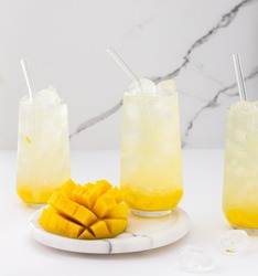 Refreshing drink with mango pulp in glasses with a glass straw on the background of a marble wall, cut mango next to the glass