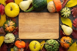 Decorative and edible pumpkin with fallen leaves of elm and maple on a green background, rectangular cutting board in the middle of the background, top view, autumn background