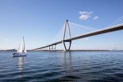 Wide angle view of Arthur Ravenel Jr. Bridge in Charleston, South Carolina, with a large sailboat floating by on a blue sky sunny day.