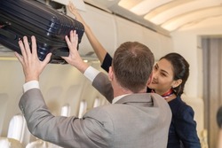 Flight attendant Young Asian woman or air hostess helping passenger place luggage in the overhead compartment on an airplane
