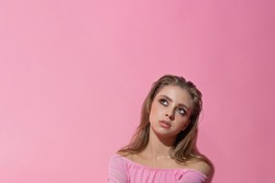 shot of a thoughtful european female with makeup looks up, contemplates a future party, dressed stylishly, follows the weekend, isolated on a pink wall. Monochrome