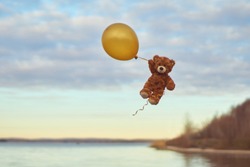 Teddy bear flying to the sky with a big yellow balloon.  A bear fly over the lake. Winnie Pooh flying with balloon.        