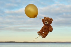 Teddy Bear flies through the sky in a yellow balloon.  Bear with yellow balloon. 