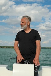 Portrait of a middle aged handsome man with grey hair on his boat on the lake