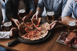 Close up of People Hands Taking Slices of Pizza. Smiling Friends Eating Pizza and Drinking Beer at Restaurant or Pizzeria. Friends Partying and Eating Pizza. Drinking Beer.