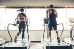 Back view of beautiful sports people running on a treadmill in gym
