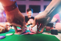 Young people play poker at the table. On the table they have glasses with alcoholic beverages, mobile phones and chips for the game. They have fun playing a game.