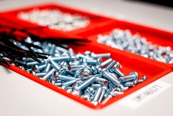 Lots of screws in a red box, factory, electronics manufacturing. Defocused