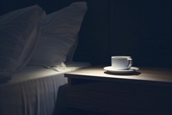 Bed side table with white mug against the bed at night time. Copy paste, nobody
