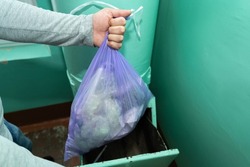 A man's hand with a garbage bag throws garbage into the garbage chute.