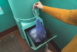 A woman's hand with a garbage bag opens the hatch of the garbage chute and throws garbage there. Close up