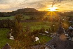 Overlooking a medieval castle, which serves as event venue just outside Maastricht and a view over the valley which is covered with rays of sun during an autumn morning just after sunrise.