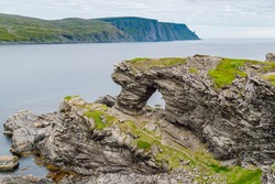 View of the Kirkeporten rock. This rock formation is a geological wonder; a fissure several metres wide in a cliff overhang shaped like a big gate, Skarsvag, Finnmark, Norway.