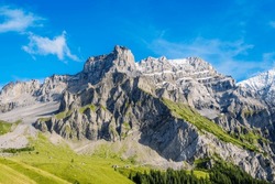 Beautiful summer alpine landscape near Adelboden, Swiss Alps. A high rocky peak at its foot traditional highland farmhouses. The peaks Hindere Loner and Mittlere Loner.