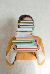 A young woman holds a stack of books in her hands.
