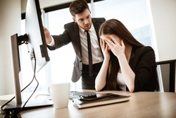 Conflict, crisis and dismissal at work. Young businessman yells at subordinate female assistant after her failure. Businessman points at monitor and fires worker. Resolving a serious work problem