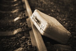 Next to the railway is an old worn-out retro suitcase, forgotten during the trip. 20th century. Immigration. Sepia.
