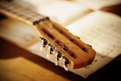 The fretboard of an old vintage acoustic guitar with metal strings lying on a wooden table next to sheets of sheet music. Solfeggio and music lessons on a sunny day. A musical instrument.