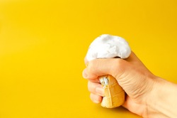 Crumpled old ice cream in a cup melts in the hands. Ice cream crushed in a fist. Ice cream in hand on a yellow background.