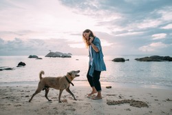 Girl has fun playing with a dog on the beach at sunset. A young European woman walks with a domestic dog on the background of the sea and the setting sun.