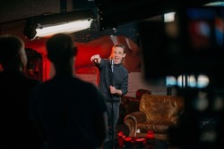 Shooting a stand-up show. Stand-up comedian on stage at the microphone. A young man, an author of jokes and comedy texts, stands on a stage in a studio during the filming of a show.