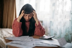 Sad woman holding her head over utility bills. The concept of rising prices for heating, gas, electricity. A young worried dissatisfied girl looks at papers does not expect a high cost of services