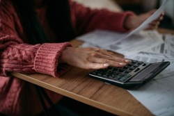 Close-up female hands with a calculator and abacus in the living room at home. A young woman calculates monthly household expenses, taxes, bank account balance and credit card bill payments.