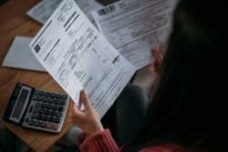 Close-up of female hands with pay slips, utility bills, account statements, payment receipts. A woman makes a count of household, family expenses with a calculator at home on the table.