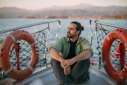 Portrait of a young man on a boat trip on a small ship in the sea on a sunny day. A Caucasian tourist guy in a summer shirt on the deck of a boat enjoys the wind in his face at sunset