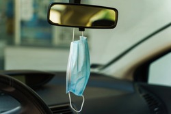 Medical protective face mask in car on the rearview mirror in day - Covid-19 pandemic protection on rear view in the vehicle - coronavirus epidemic new normal prevention concept